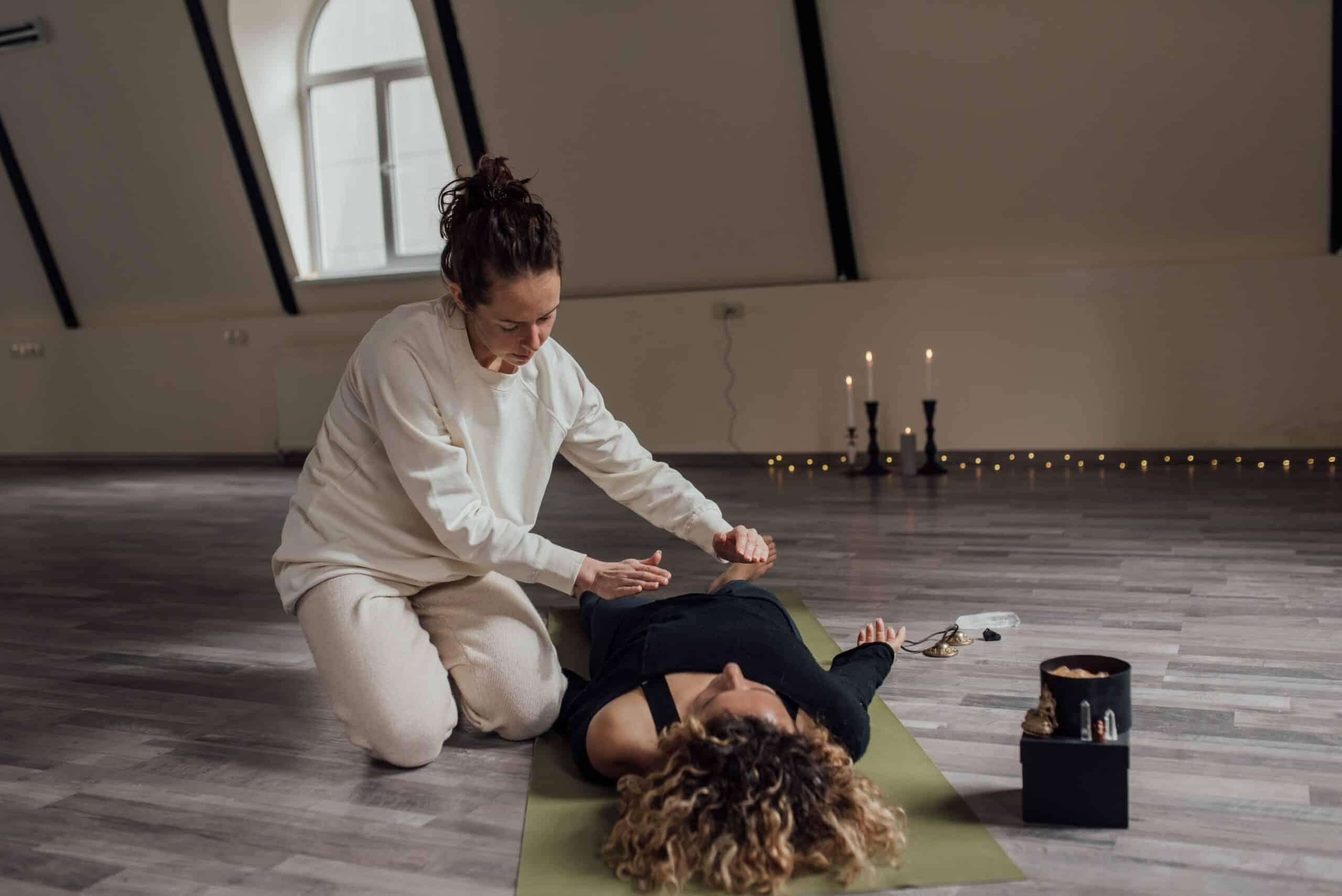 A Reiki session in a candlelit room with a practitioner attending to a relaxed recipient lying on a yoga mat